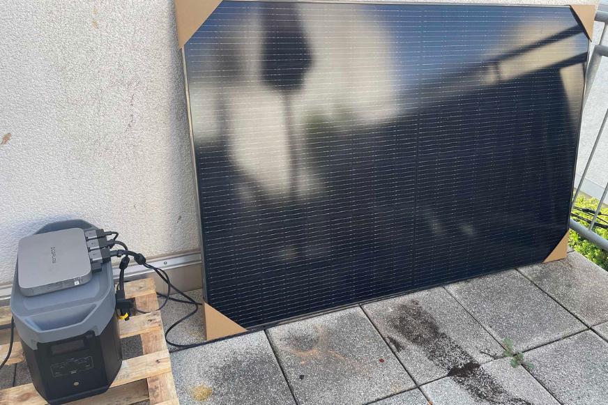 Das EcoFlow PowerStream Balkonkraftwerk steht auf dem Balkon, das Solarmodul ist an eine Wand gelehnt und der Delta 2 Max samt Wechselrichter stehen daneben und sind verkabelt.  